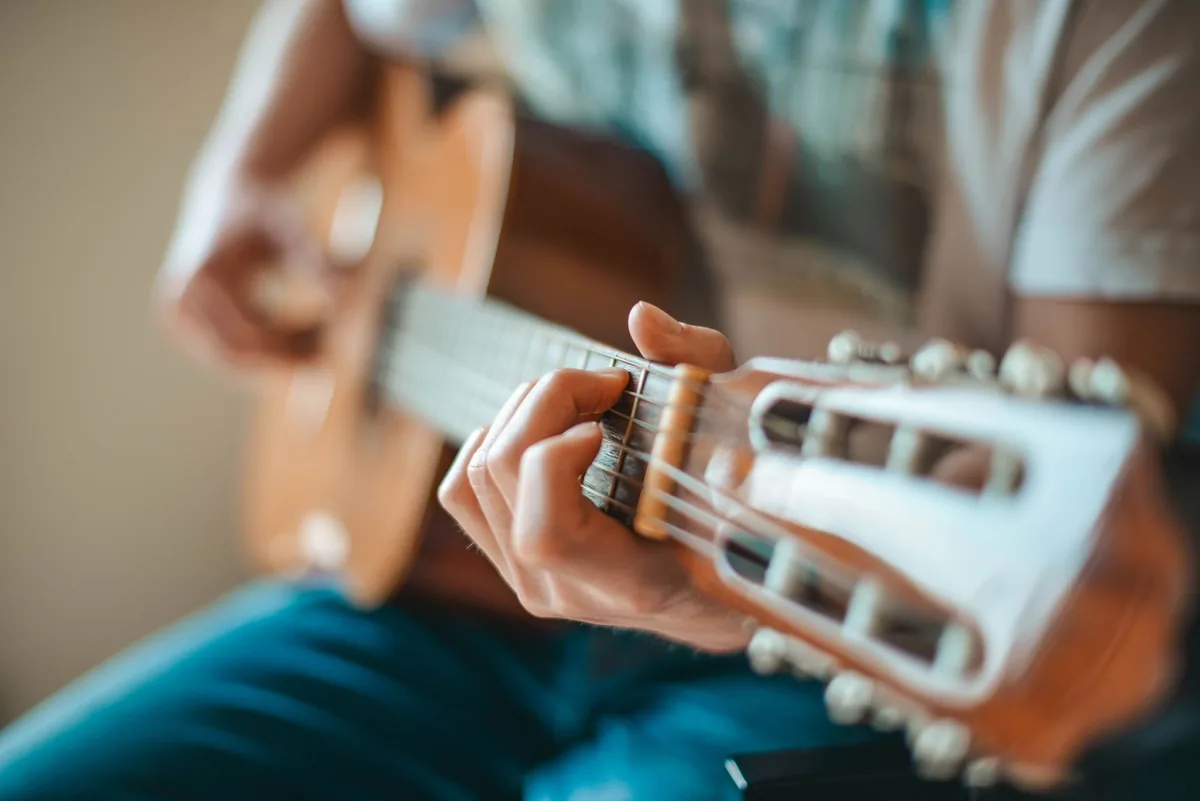 Mains jouant de la guitare acoustique en lumière chaude, évoquant le jeu d'Alain Péters