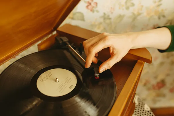 Main d'un collectionneur inspectant la surface d'un vinyle sous une lumière rasante pour évaluer son état