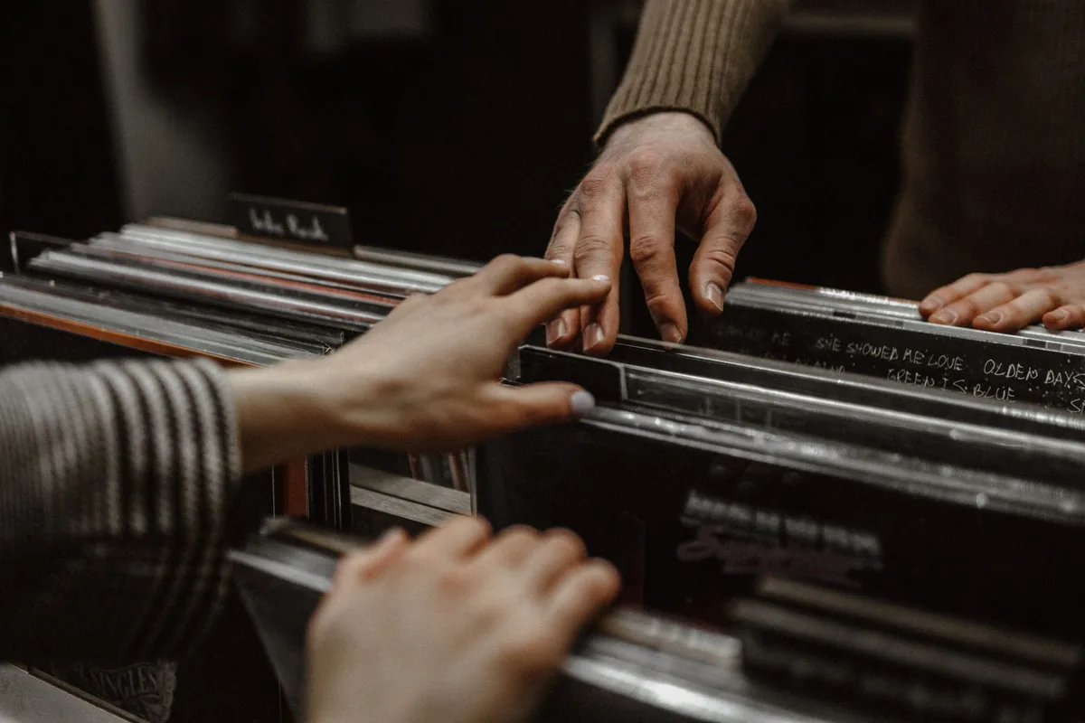 Mains feuilletant des vinyles de jazz d'occasion dans un bac de disquaire