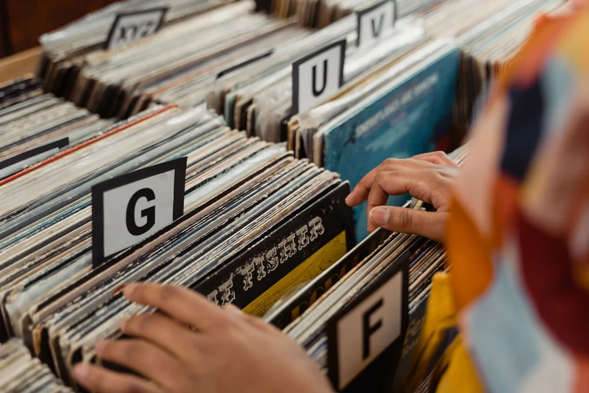 Main tenant un smartphone pour cataloguer un vinyle à côté d'une pile de disques